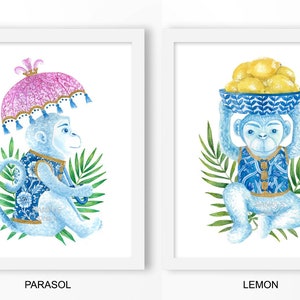 Peut inclure: Deux impressions encadrées à l'aquarelle. L'une représente un singe bleu avec un parasol rose, l'autre un singe portant des citrons dans un bol bleu. Les deux singes portent des gilets à motifs bleus et dorés, sur fond blanc avec un feuillage vert.
