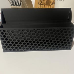 May include: A black plastic organizer with a honeycomb pattern. The organizer has two compartments and is designed to hold small items.