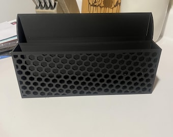 May include: A black plastic organizer with a honeycomb pattern. The organizer has two compartments and is designed to hold small items.