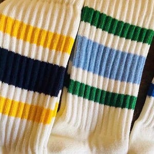 Puede incluir: Una colección de calcetines deportivos acanalados en varias combinaciones de colores. Cada calcetín presenta una base blanca con rayas diagonales en rojo, azul, amarillo, verde, naranja y negro. Los calcetines están hechos de un material suave y cómodo.