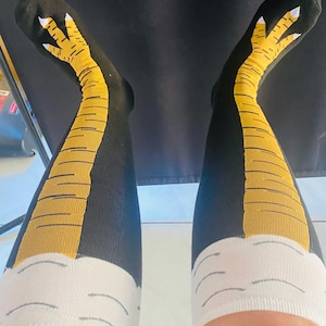 May include: A pair of black knee-high socks with a yellow and white chicken leg design. The socks have a white cuff at the top.