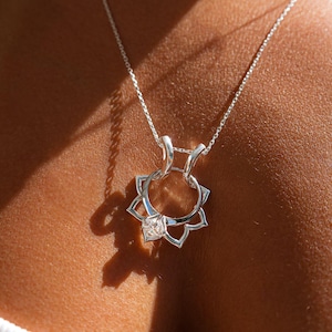 May include: A silver necklace with a pendant shaped like a lotus flower with a clear gemstone in the center.