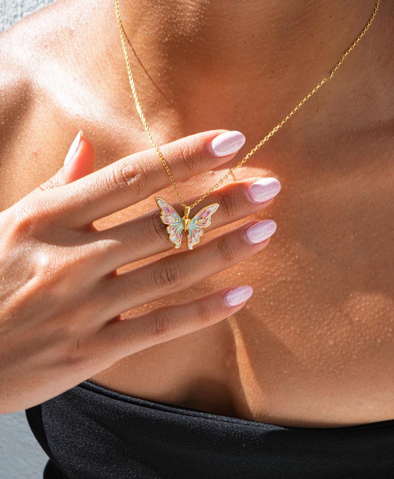 Pu&ograve; includere: Una collana con catena dorata con un ciondolo a forma di farfalla. La farfalla &egrave; realizzata in smalto bianco con accenti rosa e blu.