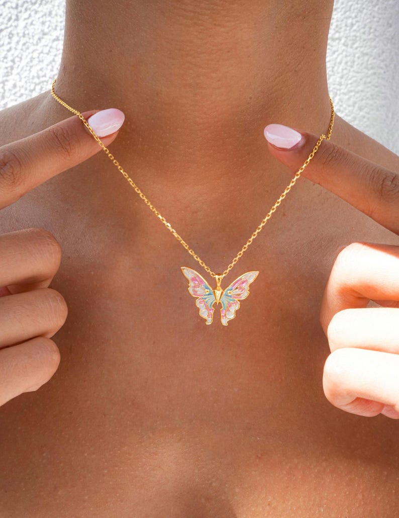 Pu&ograve; includere: Una collana con catena dorata con un ciondolo a forma di farfalla. La farfalla &egrave; realizzata in smalto bianco con accenti rosa, blu e verdi.