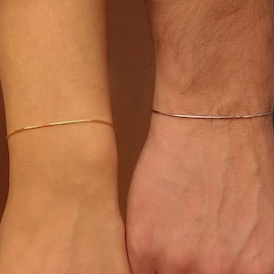 Könnte beinhalten: Zwei schlichte Armbänder, eines golden und eines silbern, an Handgelenken.
