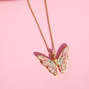 Pu&ograve; includere: Una collana con catena dorata con un ciondolo a forma di farfalla. La farfalla &egrave; bianca con accenti rosa e blu.
