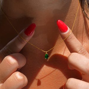 May include: A gold chain necklace with a teardrop-shaped green gemstone pendant.