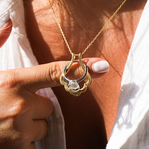 May include: A gold chain necklace with a pendant featuring two interlocking rings, one with a clear gemstone. The rings are connected by a delicate, ornate design.