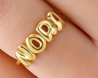 May include: Gold ring with the word "MAMA" spelled out in large, bubble-like letters.