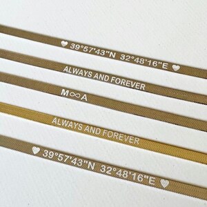 以下が含まれることがあります： 刻まれた文字が書かれた金色の金属製のバンドが4つあります。文字は「39&deg;57'43"N 32&deg;48&prime;16&Prime;E」、「ALWAYS AND FOREVER」、「MOA」、「ALWAYS AND FOREVER」です。バンドは積み重ねられており、一番上のバンドが最もよく見えます。