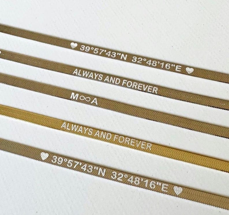 以下が含まれることがあります： 刻まれた文字が書かれた金色の金属製のバンドが4つあります。文字は「39&deg;57'43"N 32&deg;48&prime;16&Prime;E」、「ALWAYS AND FOREVER」、「MOA」、「ALWAYS AND FOREVER」です。バンドは積み重ねられており、一番上のバンドが最もよく見えます。