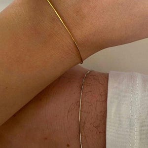 May include: Two simple gold and silver bracelets on wrists.