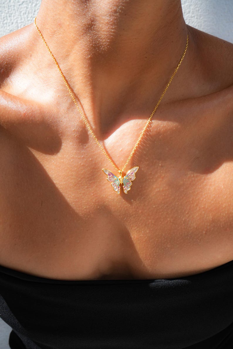 Pu&ograve; includere: Una collana con catena dorata e ciondolo a forma di farfalla iridescente.