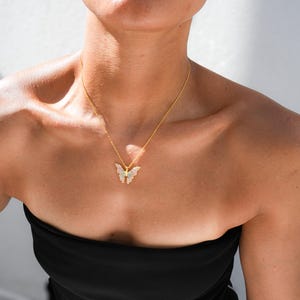 Pu&ograve; includere: Una collana con catena dorata con un ciondolo a forma di farfalla. La farfalla &egrave; realizzata in metallo bianco con strass trasparenti.