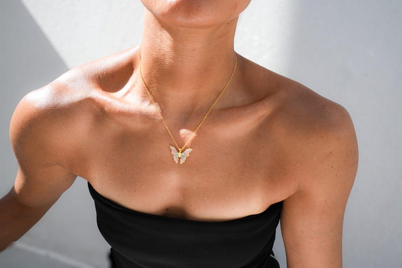 Pu&ograve; includere: Una collana con catena dorata con un ciondolo a forma di farfalla. La farfalla &egrave; realizzata in metallo bianco con strass trasparenti.