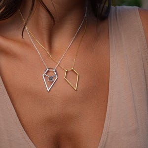 May include: Two delicate necklaces with geometric pendants. One necklace features a gold diamond-shaped pendant, while the other has a silver diamond-shaped pendant with a small ring and a clear gemstone in the center.