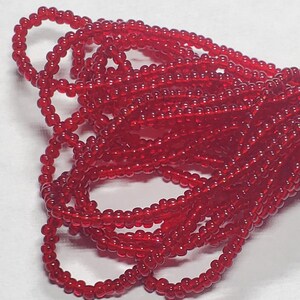 May include: A close-up of a pile of red glass seed beads. The beads are small and round, and they are arranged in a random pattern.