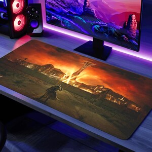 K&ouml;nnte beinhalten: Eine gro&szlig;e, rechteckige, braune und orangefarbene Gaming-Mausmatte mit einem Fallout 4-Logo und einer futuristischen Stadtlandschaft. Die Mausmatte liegt auf einem Schreibtisch mit einem Computermonitor und Lautsprechern.