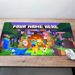 May include: A Minecraft-themed mousepad with a green, brown, and blue landscape. The text "YOUR NAME HERE" is printed in black at the top of the mousepad. There are several Minecraft characters, including Steve, a creeper, and a pig.