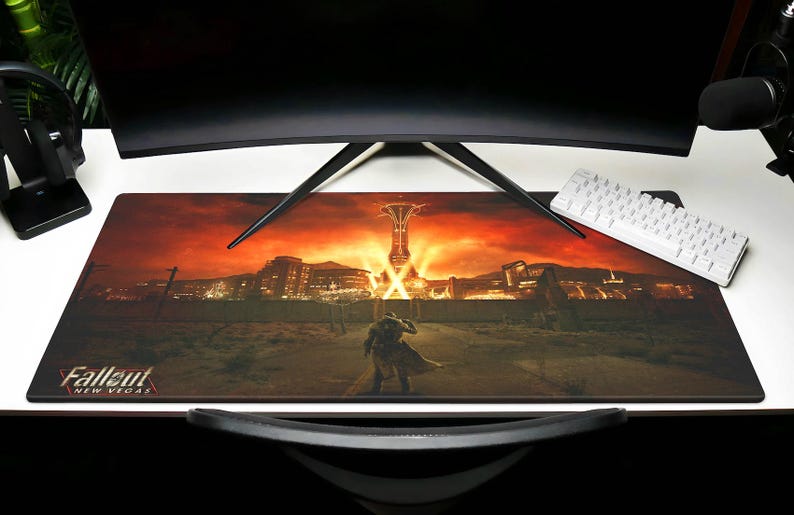 K&ouml;nnte beinhalten: Eine Fallout: New Vegas-Gaming-Mausmatte mit einem roten und orangenen Sonnenuntergangs-Hintergrund. Das Bild zeigt eine einsame Figur, die auf eine Stadt mit einem hohen Turm in der Ferne zu geht. Der Text "Fallout: New Vegas" befindet sich in der linken unteren Ecke.