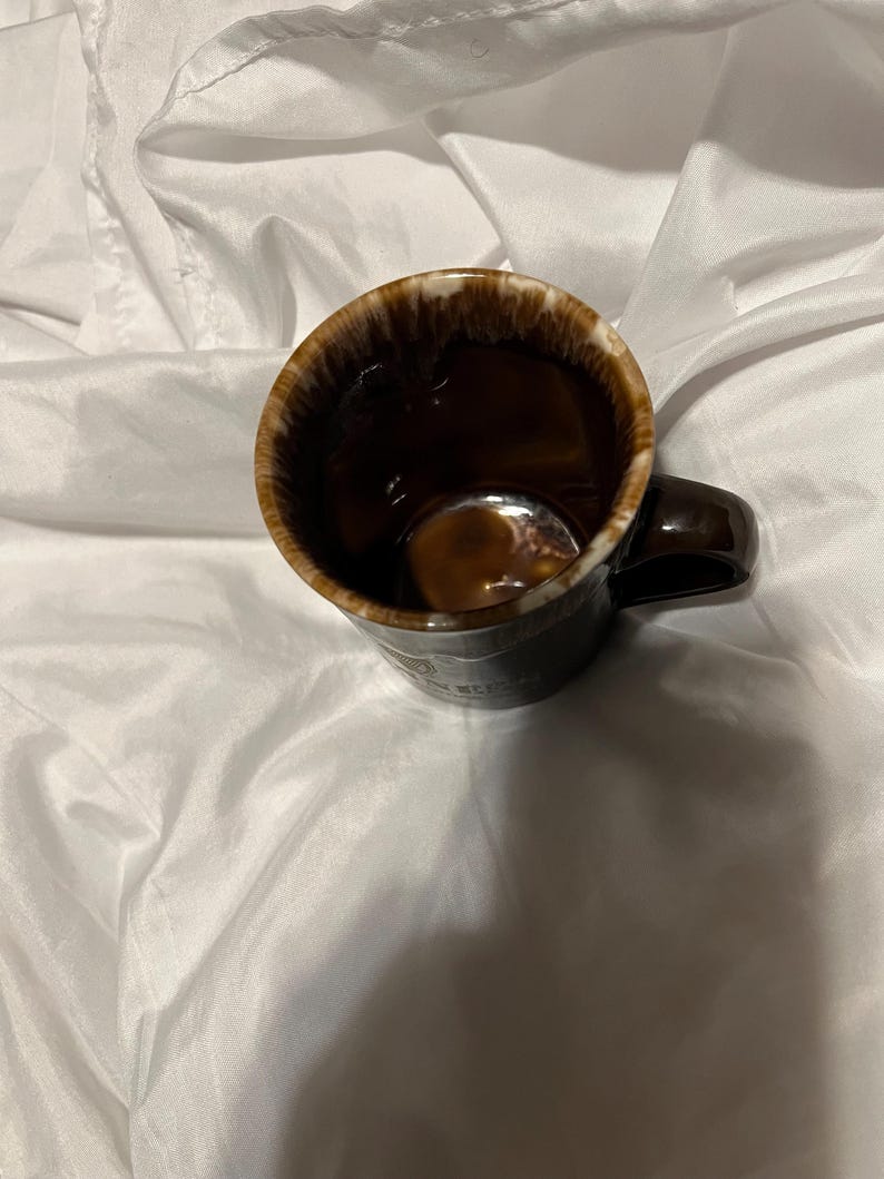 May include: A dark brown ceramic mug with a glossy finish and a distinctive drip-glaze effect around the rim, featuring a white and brown mottled pattern. The mug has a curved handle on the side and a deep, smooth interior, showcasing a classic design.