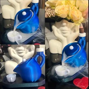 Könnte beinhalten: Eine blaue Keramik-Teekanne mit einem weißen Deckel gießt Dampf in eine weiße Teetasse. Die Teekanne steht auf einem schwarzen Tablett mit einer weißen Teetasse. Die Teekanne steht auf einer weißen Oberfläche mit einem roten Herzen.