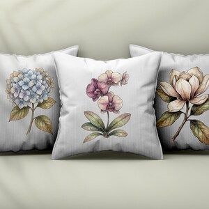 Op de afbeelding: Drie vierkante witte sierkussens met botanische illustraties. Het linker kussen toont een blauwe hortensia, het middelste kussen een paarse orchidee en het rechter kussen een cr&egrave;mekleurige magnolia bloem met groene bladeren.