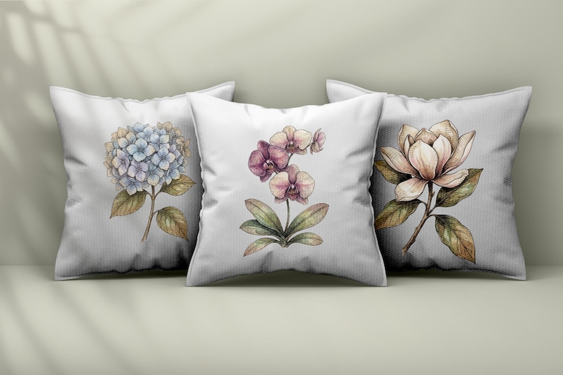 Op de afbeelding: Drie vierkante witte sierkussens met botanische illustraties. Het linker kussen toont een blauwe hortensia, het middelste kussen een paarse orchidee en het rechter kussen een cr&egrave;mekleurige magnolia bloem met groene bladeren.