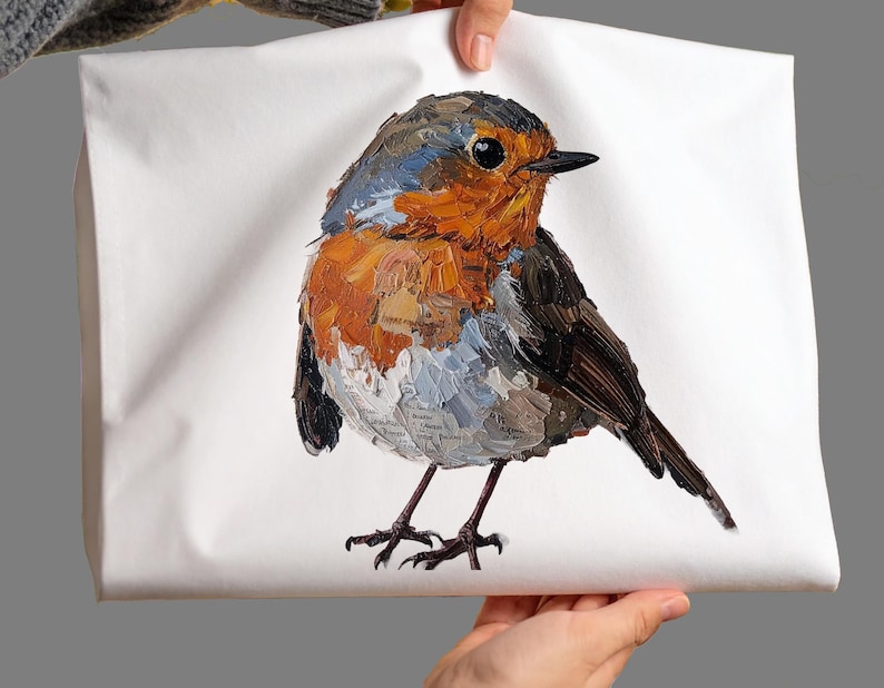 May include: A white rectangular fabric item featuring a textured, impasto-style painting of a European robin. The bird has a bright orange breast, a grey-brown head and back, and dark wings, with visible brushstrokes and small printed text details.