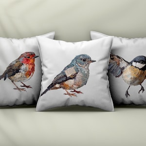 May include: Three square white throw pillows featuring detailed illustrations of birds. The left pillow shows a robin, the center pillow displays a blue-toned bird, and the right pillow depicts a black, white, and brown bird with wings spread.