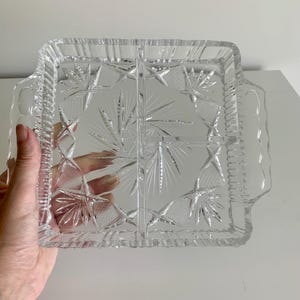 May include: A clear glass serving tray with four divided sections. The tray has a decorative cut-glass pattern and two handles.