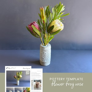 May include: A ceramic flower frog vase with a textured, vertical pattern, holding fresh protea flowers. The flowers are pink, yellow, and green. The vase is light gray and sits on a blue surface. The text "POTTERY TEMPLATE flower frog vase" is visible.