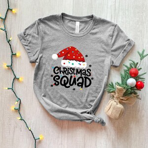 May include: Gray t-shirt with a red and white Santa hat graphic and the text "Christmas Squad".