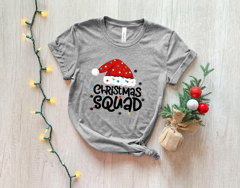 May include: Gray t-shirt with a red and white Santa hat graphic and the text "Christmas Squad".