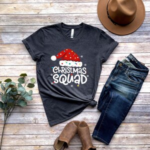 May include: A dark gray t-shirt with a white graphic of a Santa hat with colorful lights and the text "Christmas Squad".