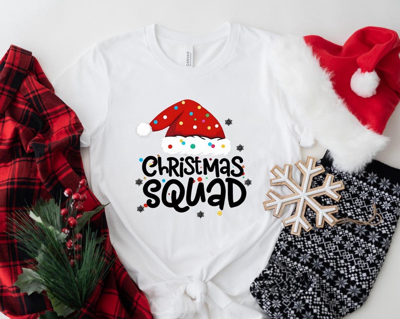 May include: White t-shirt with a red Santa hat graphic and the text "Christmas Squad" in black. The shirt is surrounded by red and black plaid fabric, a white snowflake, and a white and black patterned fabric.