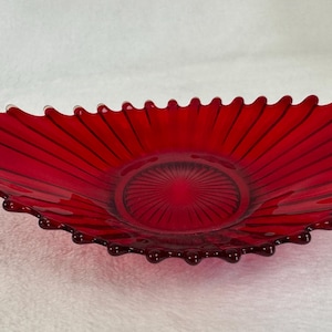 Puede incluir: Un plato de servir de vidrio rojo con un borde festoneado y un diseño acanalado. El plato tiene forma de abanico y tiene un centro profundo.