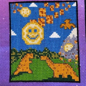Può includere: Ricamo a punto croce con un sole sorridente, dinosauri e una scena di montagna su uno sfondo di cielo blu. L'opera d'arte include colori marrone, giallo, verde, bianco e grigio, con uno sfondo viola.