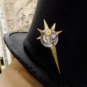 May include: A black top hat with a gold and silver steampunk-style pin featuring gears and a star shape.