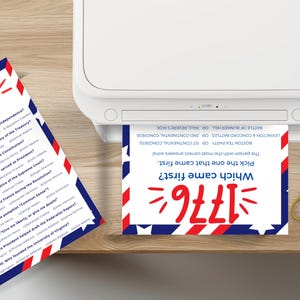 Puede incluir: Se muestra una impresora con una tarjeta de juego de trivia impresa. La tarjeta tiene un dise&ntilde;o rojo, blanco y azul con el texto "Which came first? 1776". Una segunda tarjeta est&aacute; sobre la mesa con preguntas sobre los Padres Fundadores.