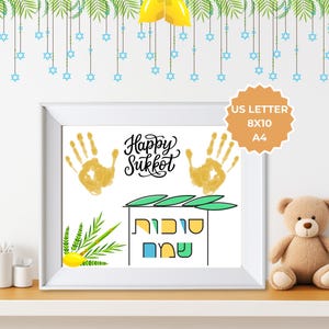 May include: A framed print with the words "Happy Sukkot" and handprints. The print includes images of a sukkah, etrog, and lulav. A small teddy bear sits on a shelf next to the framed print. The print is sized at 8x10 inches.