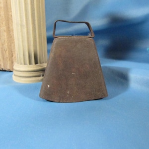 May include: A rusty metal cowbell with a simple, rounded shape and a metal handle.