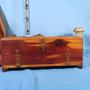 May include: A wooden box with a hinged lid and brass accents. The box is made of cedar wood and has a natural wood finish.