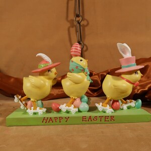 May include: Three yellow chicks on roller skates with Easter eggs. The chicks are wearing hats and one has bunny ears. The base of the figurine says "Happy Easter".