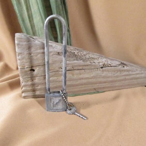 May include: A silver padlock with a key attached to it. The padlock is on a piece of driftwood.