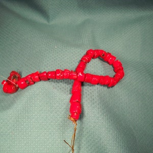 Pode incluir: Um fio de contas de coral vermelho enfiadas em um fio branco. As contas são pequenas e redondas, e o fio tem cerca de 46 cm de comprimento.