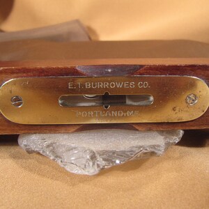 May include: A brass level with a wooden base. The level has a brass plate with the text "E.T. BURROWES CO. PORTLAND, ME".