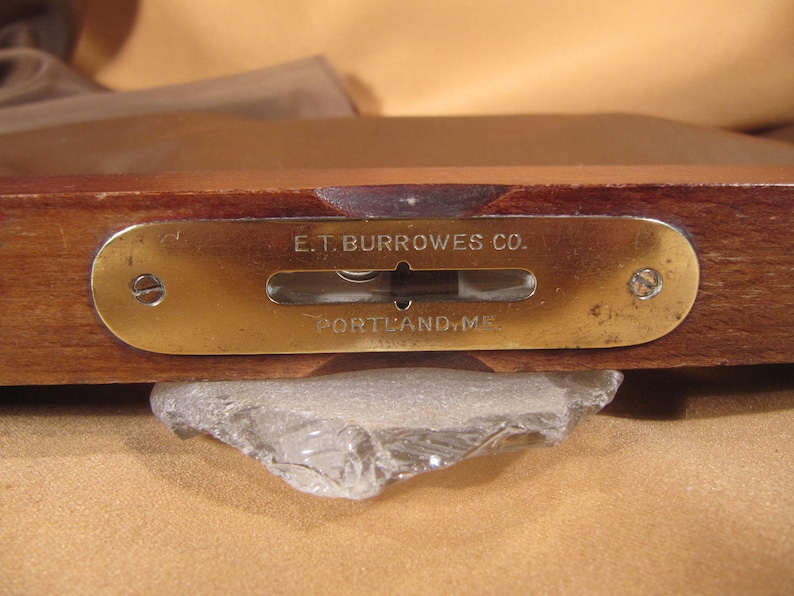 May include: A brass level with a wooden base. The level has a brass plate with the text "E.T. BURROWES CO. PORTLAND, ME".