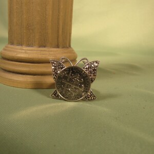 May include: Silver butterfly brooch with a United States dime coin in the center.