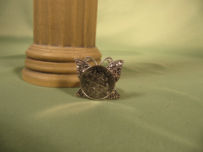 May include: Silver butterfly brooch with a United States dime coin in the center.